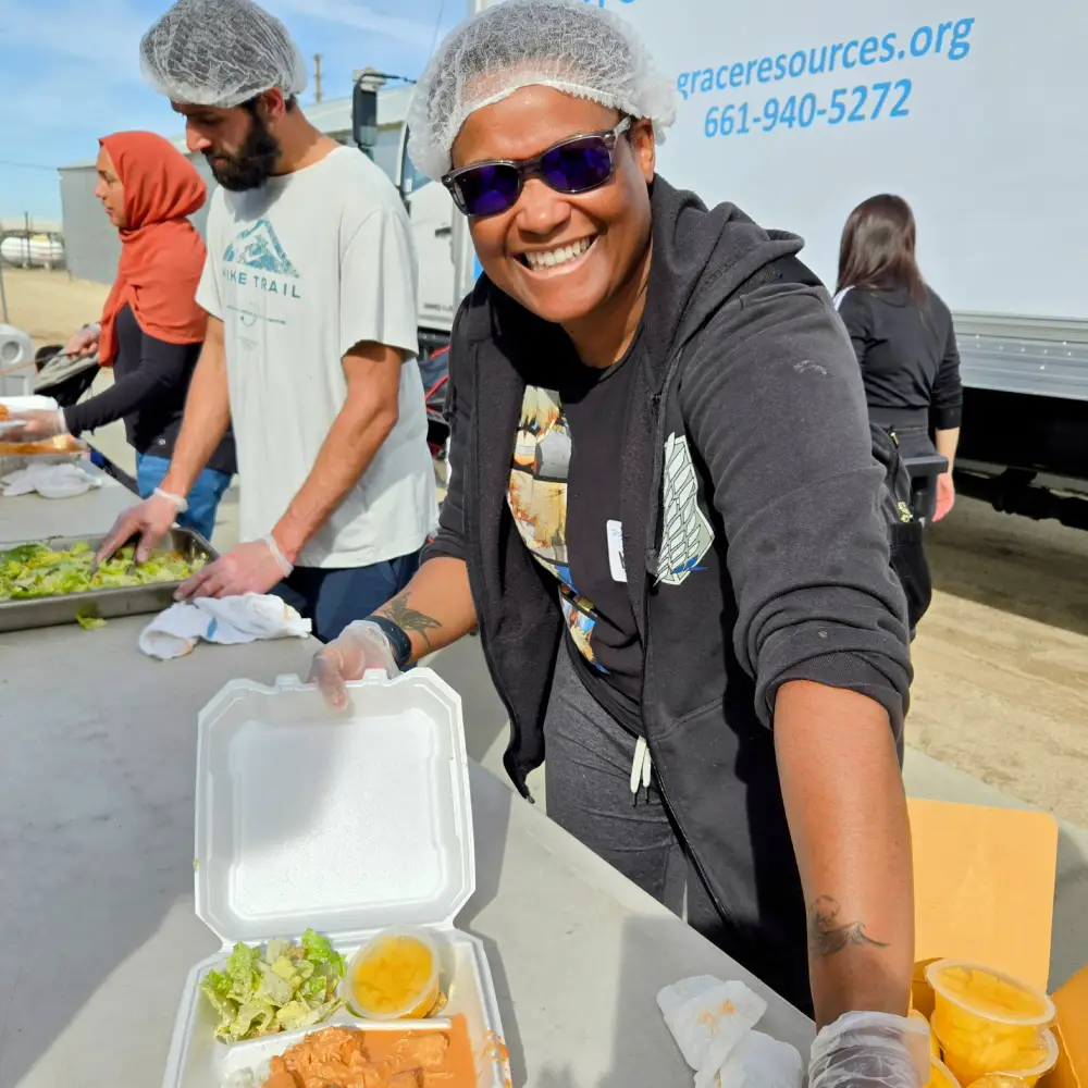 Individuals prepare and serve meals, featuring trays of salad, chicken, and sides, at a community outreach event.